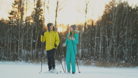 Side-view-portrait-of-active-young-couple-enjoying-skiing-in-beautiful-winter-forest,-focus-on-unrecognizable-woman-holding-ski-poles,-copy-space